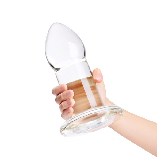 Hand holding a clear, 8-inch tapered glass anal dilator plug with a smooth surface and a wide, flared safety base.