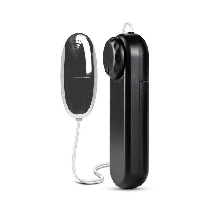The B Yours First Time Wired Remote Control Bullet Vibrator by Blush is a small, oval-shaped black and metallic silver gadget connected to a handheld remote control device by a thin wire. The black remote features a circular dial at the top for adjusting multispeed settings, ideal for clitoral stimulation, all against a white background.