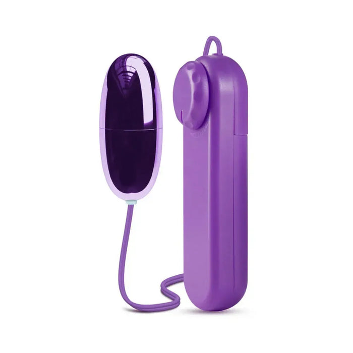 The B Yours First Time Wired Remote Control Power Bullet Vibrator in purple from Blush is depicted. Its sleek, oval-shaped body promises exquisite clitoral stimulation and is connected by a cord to a rectangular remote control featuring a dial and convenient loop for easy handling.