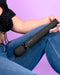 A person seated holding a large black Le Wand Powerful Cordless Vibrator, a powerful sex toy, against a purple background.
