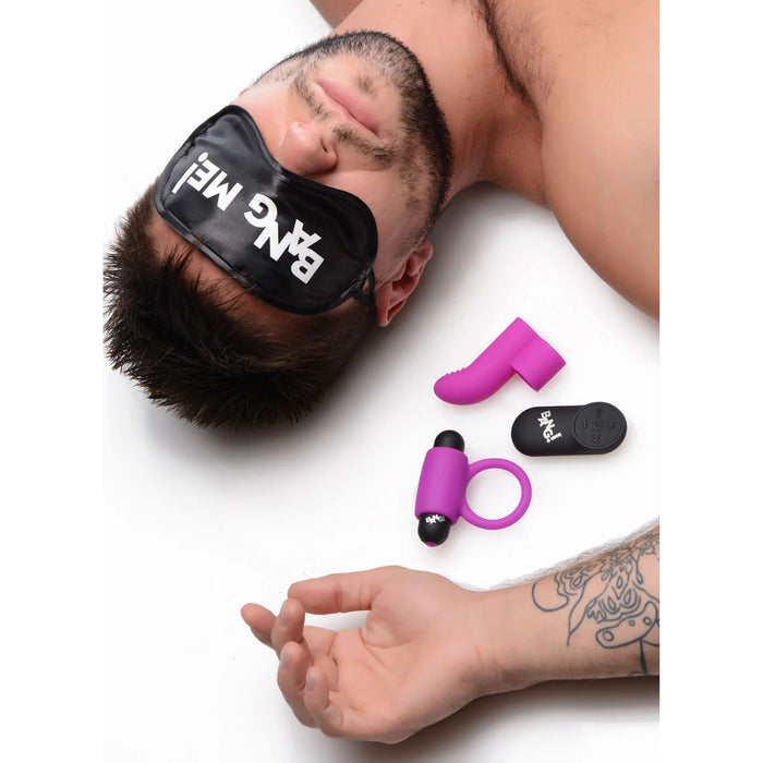 A topless man lies on a white surface wearing a black eye mask inscribed with "BANG ME!" from the BANG! Couple's Cock Ring, Finger Vibe, Bullet & Blindfold Kit - Purple by XR Brands. Beneath his arm, there are three purple and black sex toys from the kit, including a vibrating bullet. A tattoo is visible near his right wrist.