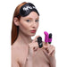A woman with long red hair is wearing a black BANG! blindfold from the XR Brands kit, which features white text that reads "BANG ME." She is holding a remote control in one hand and a small black and purple remote-controlled vibrating bullet from the BANG! Couple's Cock Ring, Finger Vibe, Bullet & Blindfold Kit - Purple in the other.