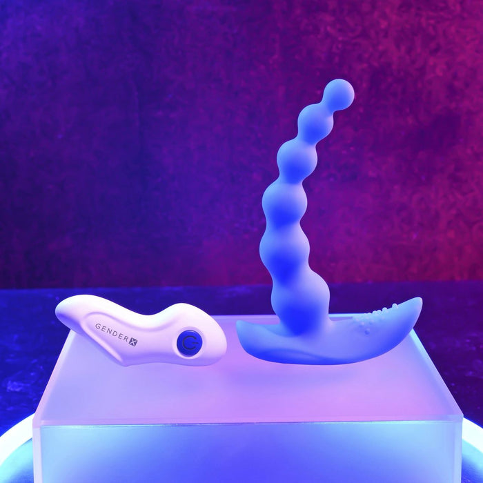 The Beaded Pleasure Remote Control Vibrating Anal Beads by Evolved Novelties, featuring a blue, silky silicone construction and a textured base, are elegantly displayed on a clear, luminous platform. The background showcases a gradient of purple and red hues, creating a futuristic and vibrant ambiance.