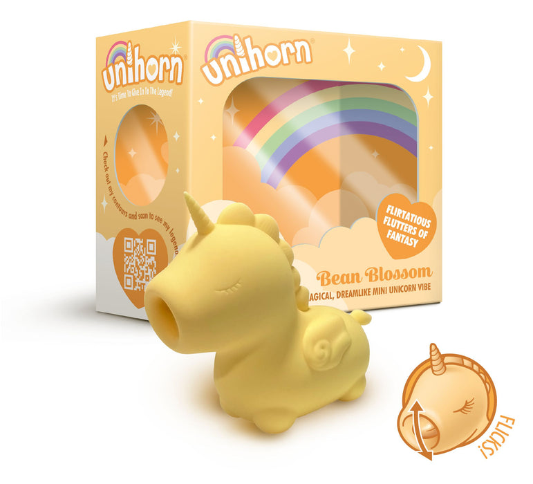 A small, yellow Bean Blossom Unicorn Shaped Licking Tongue Vibrator from Creative Conceptions is placed in front of its colorful packaging that features a rainbow design. The package includes the text "Unicorn," "Bean Blossom," and "Flirty Flutters of Fantasy." An orange sticker with the word "Exclusive" is visible in the corner of the image.