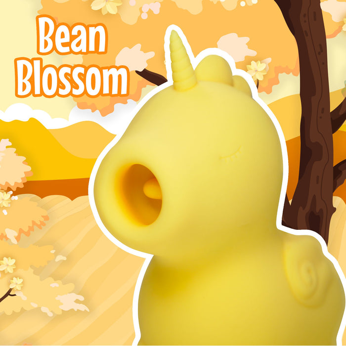 A charming yellow unicorn character with a petite horn and serene closed eyes, set against a whimsical autumn-themed backdrop featuring trees and leaves in warm shades of orange and yellow. The text "Bean Blossom" appears in the top left corner, showcasing the Bean Blossom Unicorn Shaped Licking Tongue Vibrator - Yellow by Creative Conceptions. Its soft silicone finish is ideal for cozy fall vibes.
