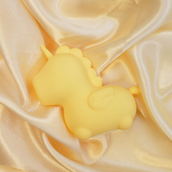 A Bean Blossom Unicorn Shaped Licking Tongue Vibrator - Yellow from Creative Conceptions lies on a smooth, luxurious, golden fabric. The fabric has a satiny sheen and cradles the toy in its folds. Made from premium silicone for a soft touch, the vibrant unicorn features a simple, rounded shape with minimal detail.