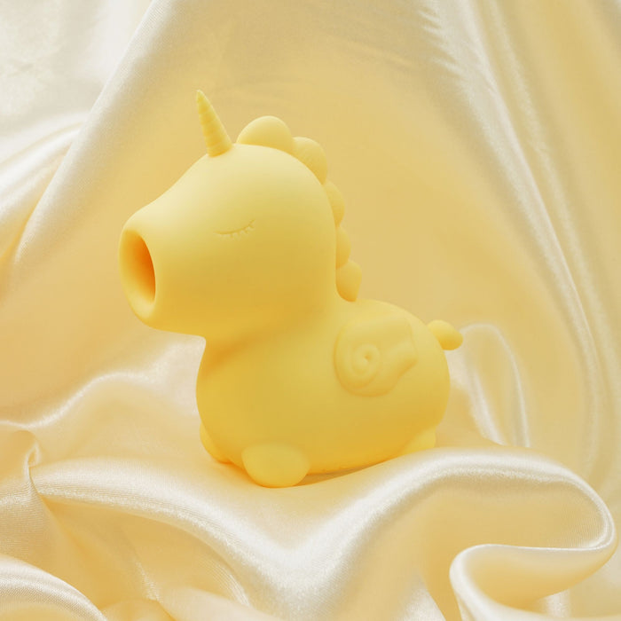 The Bean Blossom Unicorn Shaped Licking Tongue Vibrator in yellow, by Creative Conceptions, is a small, smooth figurine with closed eyes and a simple horn. It sits on a draped, glossy white fabric background, creating a soft and calming aesthetic. Crafted from premium silicone, its round shape and minimalist design give it a whimsical and friendly appearance.