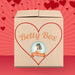 A cardboard pleasure box with a large red heart outline and "Betty's Penis Pleasures Mystery Box - Valentine's 2026 Edition" on the front. Set against a red background with hearts, it features a retro woman logo, hinting at surprises inside.