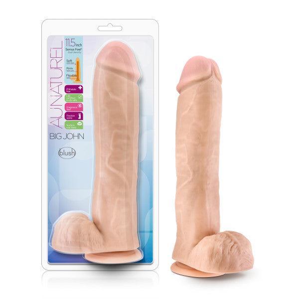The image features "Big John," a realistic-looking, vanilla-colored dual density dildo from Blush, standing upright with a suction cup base. The clear plastic packaging in the background showcases product information, including 11.5 inches in size, softness, and flexibility.