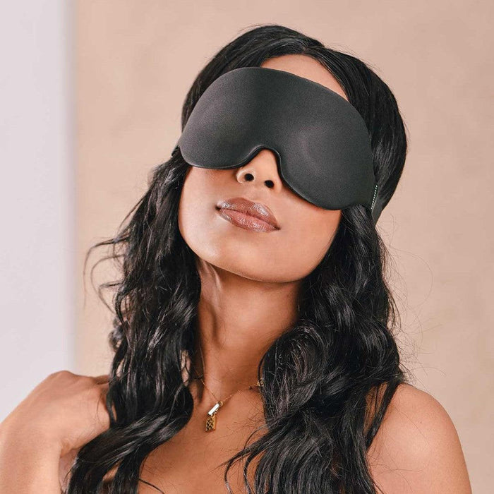 A woman with wavy hair wearing a Blackout Blindfold by Sportsheets in a serene pose.