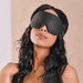 A woman with wavy hair wearing a Blackout Blindfold by Sportsheets in a serene pose.