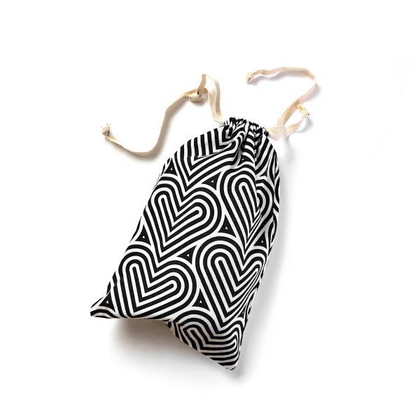 Introducing the Blush Bomba Black & White Hearts Sex Toy Storage Bag by Blush— a stylish black and white drawstring bag featuring a geometric pattern of interlocking heart shapes, ideal for discreetly storing your sex toys. The beige drawstrings are knotted at the ends, adding a chic touch. Machine washable and lint-free, this bag is shown positioned diagonally on a plain white background.