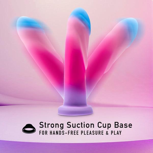 A photo of the Borealis Dreams 7.75 Inch Girthy Silicone Dildo - Cotton Candy by Blush, featuring a pastel-colored design with hues of pink, blue, and purple. The dildo has a three-pronged structure and comes with a strong suction cup base for hands-free pleasure and play. The background is shaded in light pink and purple.