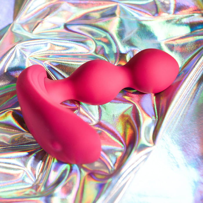 The Bubble Butt Inflatable Vibrating Butt Plug with Remote from Evolved Novelties, a pink, body-safe silicone pleasure product with a curved, bulbous design, is set against a shiny, iridescent background. The reflections of various colors create a vibrant and playful atmosphere in the image.