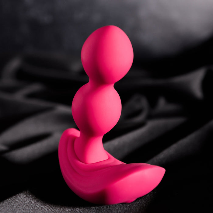 The Bubble Butt Inflatable Vibrating Butt Plug with Remote from Evolved Novelties, featuring a bright pink, curved silicone body-safe design with two rounded bulbs and a wide, contoured base, is showcased against a dark, textured fabric backdrop. The toy's smooth surface and modern design are accentuated by the dramatic lighting.