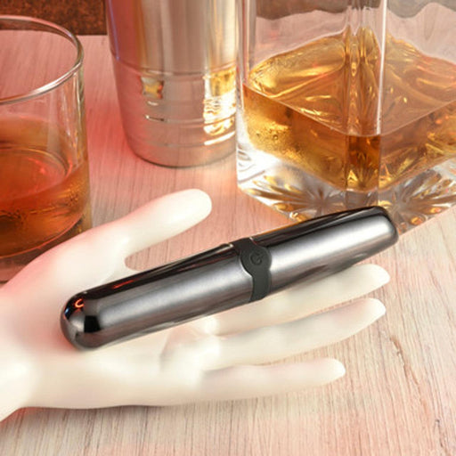 A Buzz Buddy Powerful Metal Vibrator by Evolved Novelties rests on a white mannequin hand placed on a wooden surface. Behind it, there's a glass tumbler filled with amber liquid and a decanter containing a similar beverage, suggesting a casual or relaxed setting—perfect for unwinding with your beginner-friendly vibe.