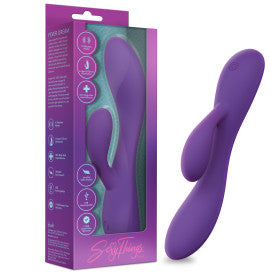 The Fever Dream Beginner G-Spot Rabbit Vibrator in purple silicone is shown beside its purple and teal packaging, which displays product info and the "Sexy Things" brand name in cursive at the bottom.