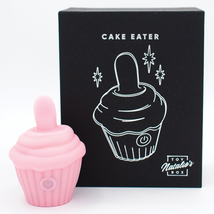 The pink Cake Eater Clitoral Stimulator Tongue Vibrator stands beside its black box packaging, which displays a white line drawing and the product name, promising indulgent clitoral stimulation.
