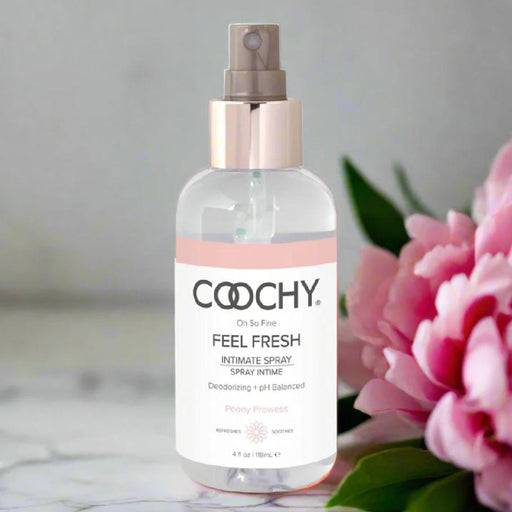 A clear Coochy Intimate Feminine Spray - Peony Prowess 4 oz sits beside a pink peony on a light surface, showcasing its pH-balanced feminine deodorant formula against a softly blurred background.