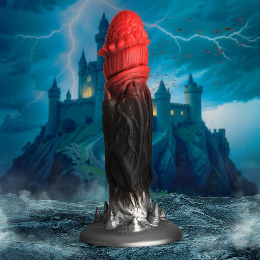 The Count Cockula Vampire Fantasy Silicone Dildo by XR Brands features a dark, fantasy-themed design. Crafted from premium silicone, it stands on a rocky base. The top half of the dildo is red and resembles a menacing dragon's head, while the bottom half transitions to black with spiky protrusions. In the background, there's a stormy sky and a castle perched on a hill.