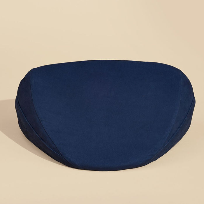 A Dame Pillo Sex Pillow for Sex Positioning - Indigo placed against a beige background. The cushion, reminiscent of a wedge-shaped pillow, has a flat top and a slightly elevated, supportive outer edge, designed for comfortable seating during meditation or yoga practices.