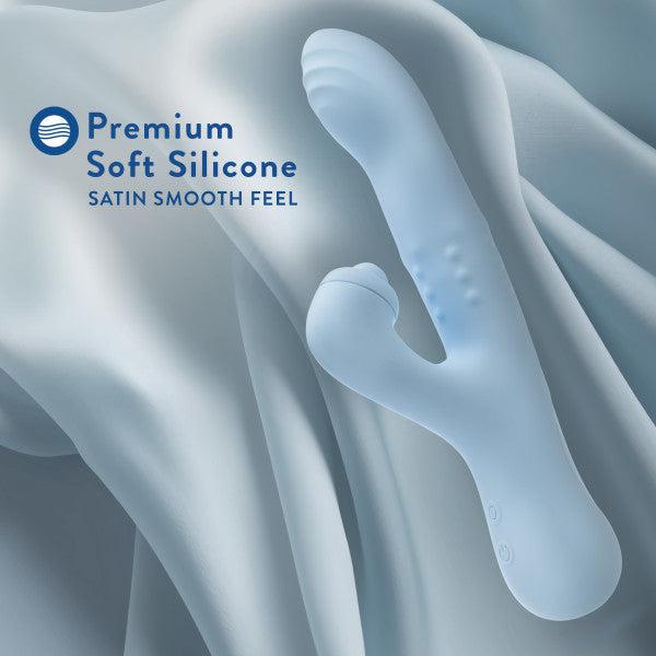 Displayed on a silky fabric background, the Devin Clit Thumping G-Spot Rabbit with Shaft Rotation by Blush is showcased in its blue silicone form. Featuring a curved design and textured surface, this massager offers dual stimulation to ensure maximum pleasure. The text "Premium Soft Silicone Satin Smooth Feel" is featured in the top left corner.