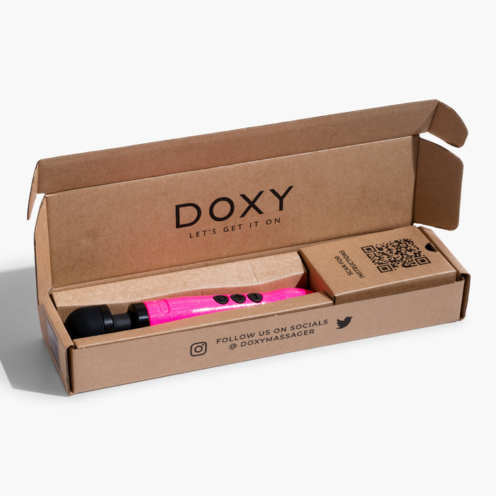 A hot pink Doxy Die Cast 3 Compact Wand Vibrator, celebrated for its targeted intensity, is showcased inside an open cardboard box. The box displays the Doxy logo and the slogan "Let's Get It On" printed on the inside lid, with a QR code and social media handle @DoxyMassager.
