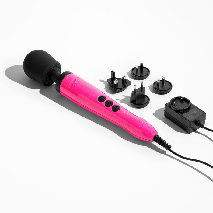 The Doxy Die Cast Extra Powerful Wand Vibrator in Hot Pink, known for its deep rumbly vibrations and featuring a black rounded head with a power cord, is laid out on a white surface alongside five black plug adapters and a black power adapter.
