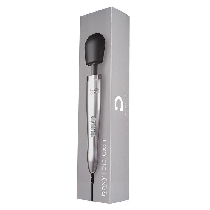 A sleek, silver-colored luxurious wand vibrator with a black head, known as the Doxy Die Cast Extra Powerful Wand Vibrator - Silver, is displayed vertically next to its matching gray box packaging. The box features branding text that reads "DOXY." The massager, designed for deep rumbly vibrations, has three buttons on its handle and a cord at the bottom.