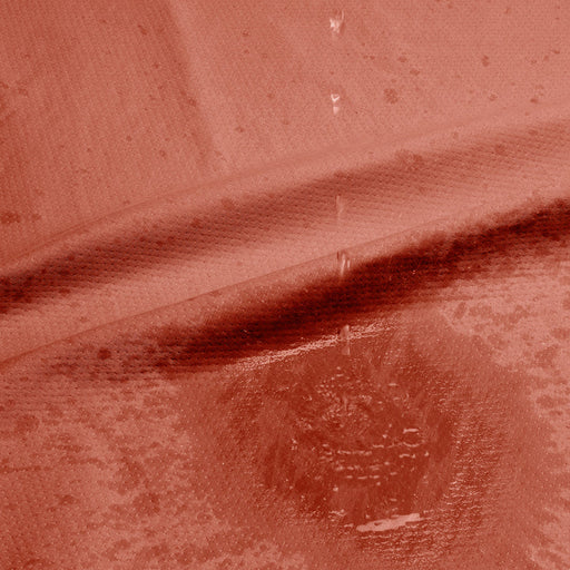 Close-up of water droplets on a textured red surface, forming a spreading stain—perfectly captured on the Dame Thro Soft Waterproof Sex Blanket, which is ultra-soft, machine washable, and fully waterproof.