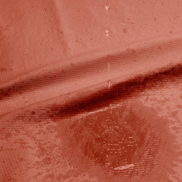 Close-up of water droplets on a textured red surface, forming a spreading stain—perfectly captured on the Dame Thro Soft Waterproof Sex Blanket, which is ultra-soft, machine washable, and fully waterproof.