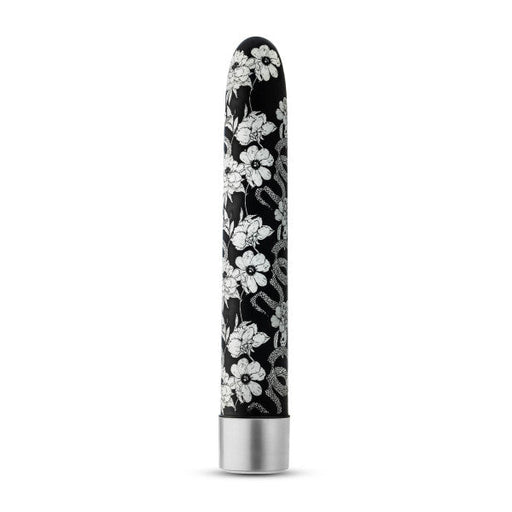 The Eden Black Floral Slim Beginner Bullet Vibrator by Blush features a sleek, black cylindrical design adorned with intricate white floral patterns. Its metallic silver base contrasts beautifully with the elegant floral surface, allowing the classic slimline vibrator to stand upright against a plain white background and offering powerful vibration modes.