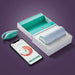 The Elvie Trainer Smart Kegel Exerciser in teal and white sits beside its open case and a smartphone showing progress charts, all placed on a purple surface.