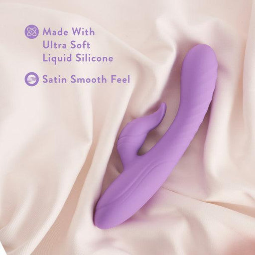 An Evelyn Beginner G-Spot Rabbit Vibrator in purple from Blush, designed with an ergonomic curve and a smaller protrusion, lies on soft cream-colored fabric. The text to the left reads "Made With Ultra Soft Liquid Silicone" and "Satin Smooth Feel," accompanied by matching icons, promising optimal clit stimulation.