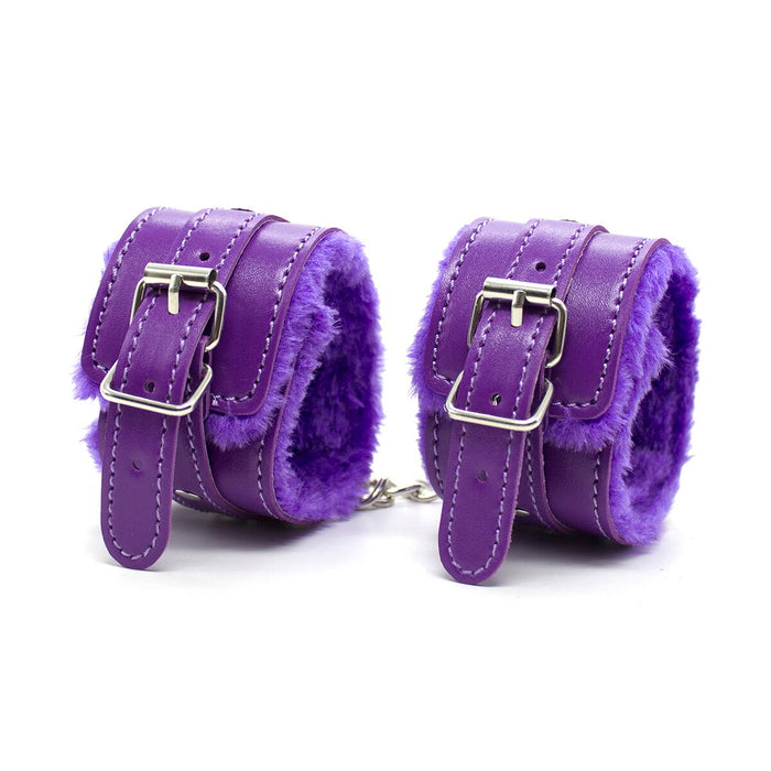 Two purple leather handcuffs from the Everything Bondage 9 Piece Beginner's Bondage Kit by Ple'sur, lined with soft, fuzzy purple fabric, are connected by a short silver chain. Each cuff features a metal buckle closure and multiple adjustment holes. Perfect for a sensory thrill, the cuffs are positioned upright, side by side, against a white background.