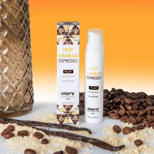 A bottle and box of Exsens Cooling Vanilla Espresso Flavored Arousal Gel (15ml), a sensual pleasure enhancer, are shown with coffee beans, vanilla beans, and cookie crumbs on an orange gradient background.