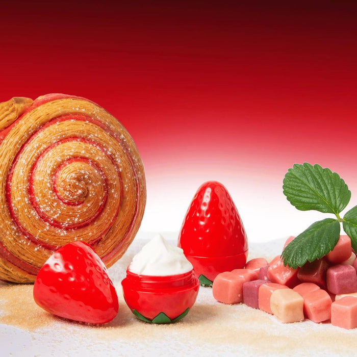 A swirl pastry, Exsens Oh My Strawberry Flavored Nipple Arousal Cream (8ml) in strawberry-shaped lip balm containers, small pastel candies, and a green strawberry leaf are arranged on sugared sprinkles against a red gradient backdrop.