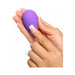 A person's hands holding the Fantasy For Her Remote Controlled Kegel Exerciser by Pipedream Products, which is small, purple, and egg-shaped with a power button near the top. One finger with a French manicure is pressing the button against a white background.