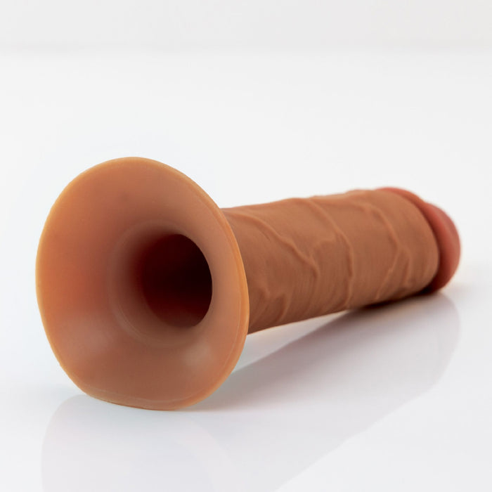 A chocolate-colored, textured silicone object, resembling the Fantasy X-Tensions Elite Hollow 7 Inch Silicone Dildo & Strap-On Harness from Pipedream Products, with a flared base and cylindrical shape, is shown on a plain white background.