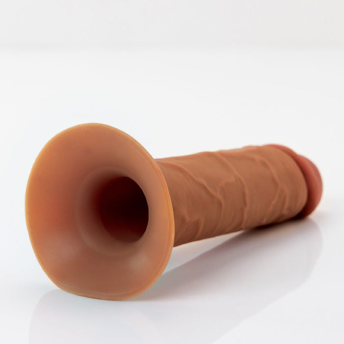 The Fantasy X-Tensions Elite Hollow 8 Inch Silicone Dildo & Strap-On Harness by Pipedream Products lies horizontally on a white surface. This chocolate-colored, realistic dildo features detailed textures and contours for a lifelike appearance, with a wide suction cup base making it an ideal erectile dysfunction solution.