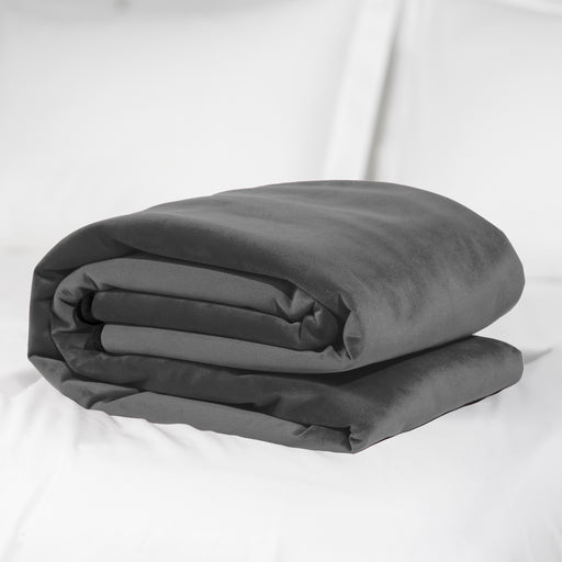 A neatly folded Liberator Fascinator Throw King Size Waterproof Sex Blanket in dark gray rests on a white bed with white pillows in the background.
