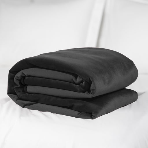 A neatly folded Liberator Fascinator Throw Queen Size Waterproof Sex Blanket in black is placed on a white bed with white pillows in the background.