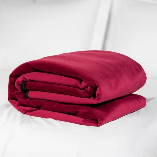 The Liberator Fascinator Throw Queen Size Waterproof Sex Blanket, in deep red, is neatly folded and placed on a white bed with white pillows in the background.