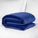 A neatly folded Liberator Fascinator Travel Sized Waterproof Sex Blanket in deep blue sits on a white bed with white pillows in the background.