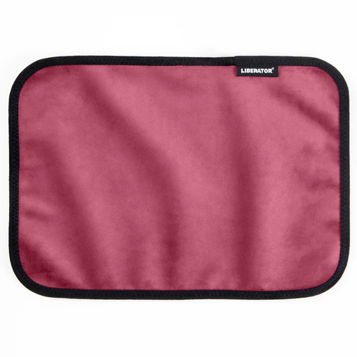 The Liberator Fascinator Toy Pad – Moisture-Proof Mini Mat is a rectangular, rose-colored microfiber pad with black trim and a small "LIBERATOR" tag. This machine-washable mat is shown on a white background.