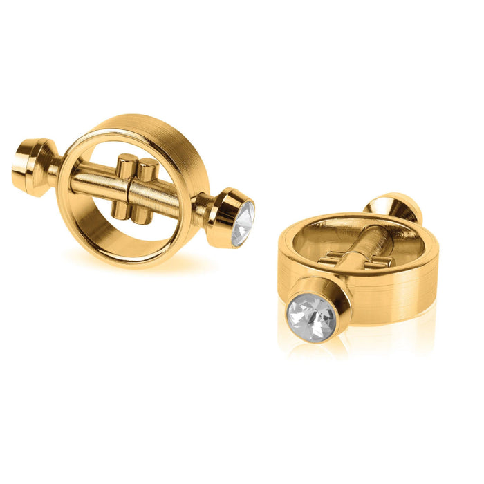 The Fetish Fantasy Gold Magnetic Nipple Clamps with Diamond Tips by Pipedream Products feature an elegant design with a central bar adorned with faux diamonds at each end. One clamp lies flat, while the other stands upright, showcasing different angles in polished gold.