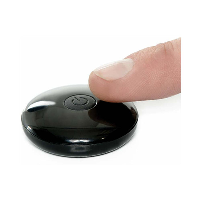 A close-up image shows a finger pressing the power button on a small, round, black component of the Fetish Fantasy Vibrating 10 Inch Hollow Dildo & Strap-on Harness - Caramel by Pipedream Products. The component is smooth and shiny with a slightly domed surface, reminiscent of polished medical equipment used for addressing issues like erectile dysfunction. The power symbol is clearly visible at its center.