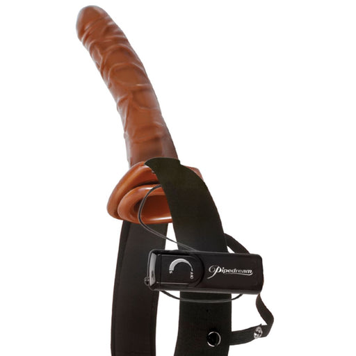 Introducing the Fetish Fantasy Vibrating 10 Inch Hollow Dildo & Strap-on Harness - Chocolate by Pipedream Products. This innovative product features a brown, flexible strap-on harness and an adjustable black strap with an elastic fit. The control module labeled "Pipedream" includes a dial for seamless operation and is conveniently attached to the harness.