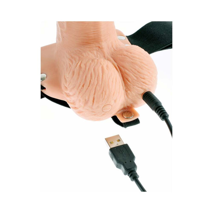 A close-up image depicts the Fetish Fantasy Vibrating 6 Inch Hollow Dildo with Balls and Strap-on Harness with Remote in Vanilla from Pipedream Products. The realistic model is attached to a USB cord, suggesting it may be used for educational or novelty purposes, such as aiding those with erectile dysfunction. The black USB cord is connected to the base of the dildo.