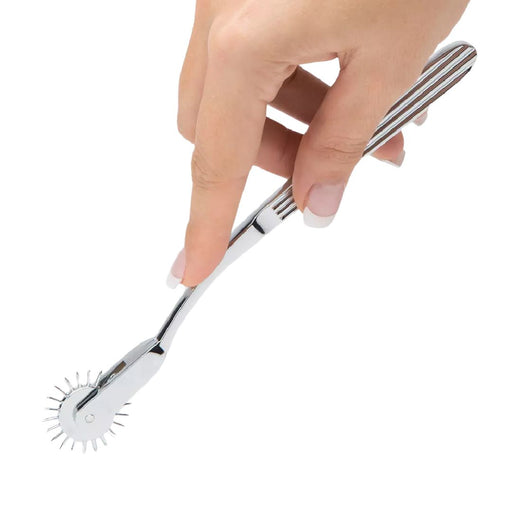 A hand is holding a silver Fifty Shades Darker Adrenaline Spikes Metal Wartenberg Pinwheel by Lovehoney against a white background. The tool, often found among sensory toys, features a wheel with small, evenly spaced spikes at the end, typically used in sensory testing or for culinary purposes.